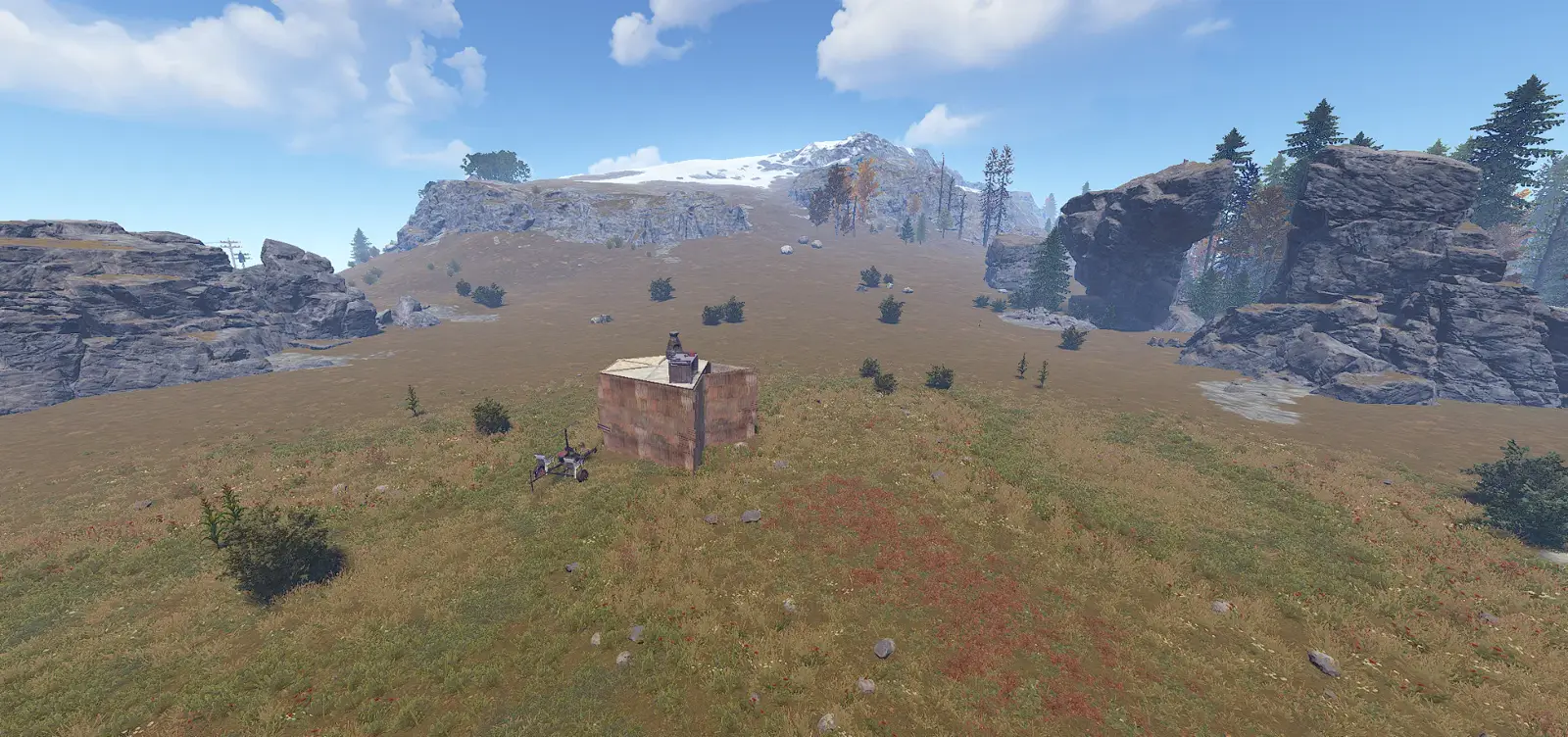 A small metal base with a minicopter on a grassy plain below a snowy peak